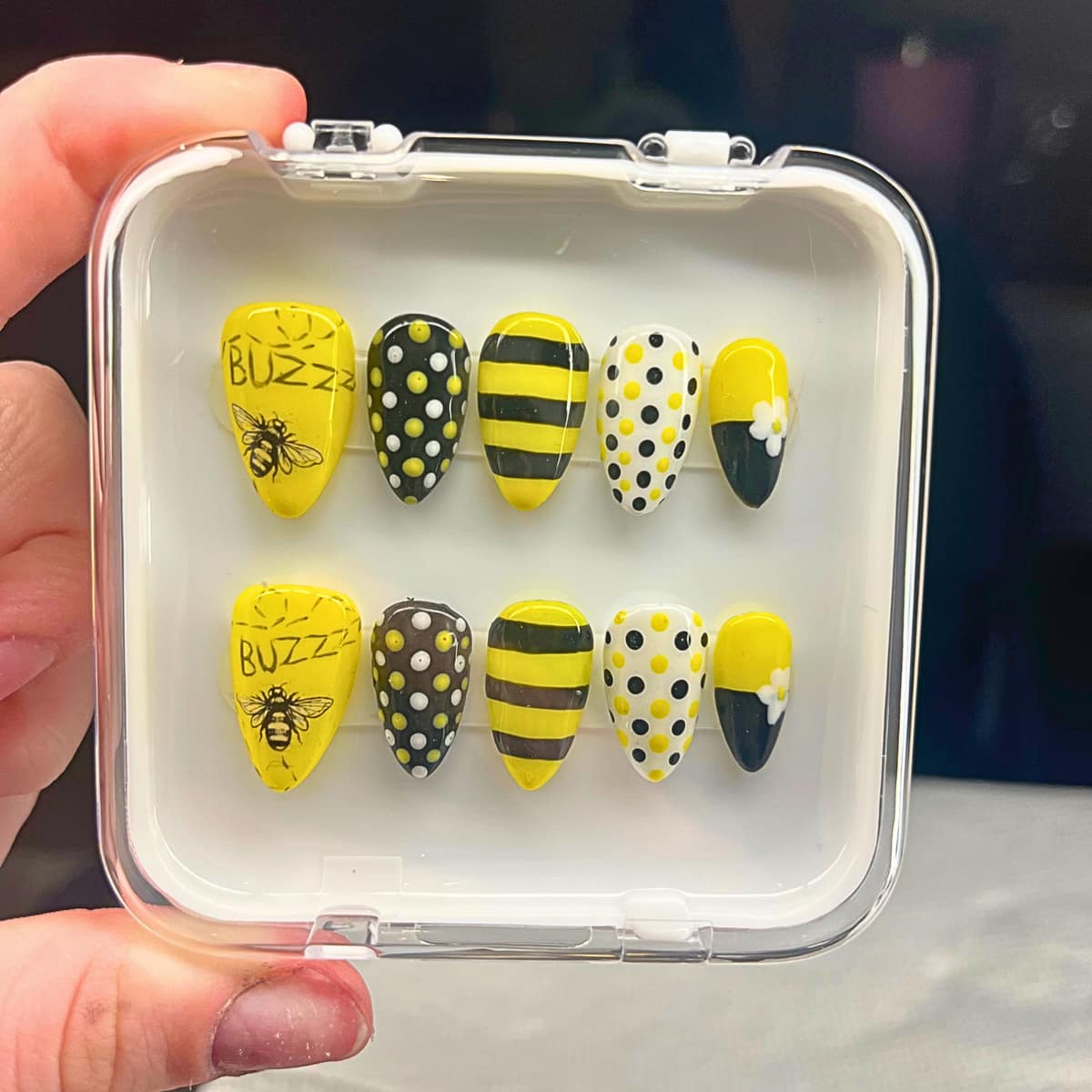 Boxed press-on set in yellow and black — bees, stripes, dots, and a white daisy.