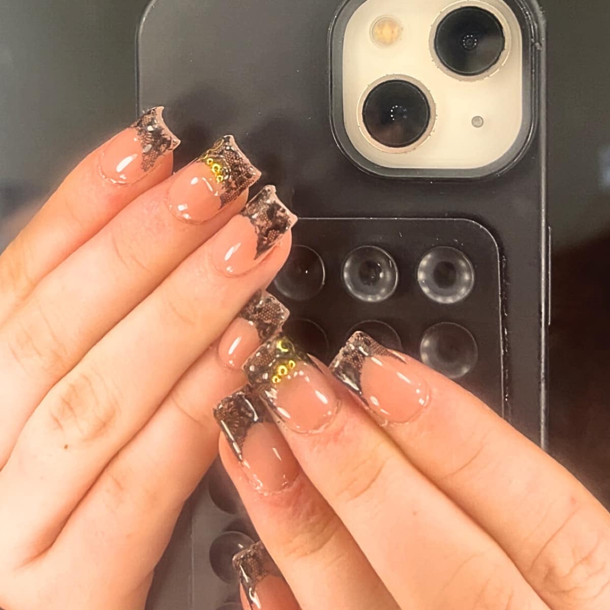 Square tips edged in black lace over a bare nail, finished with small gold beads.
