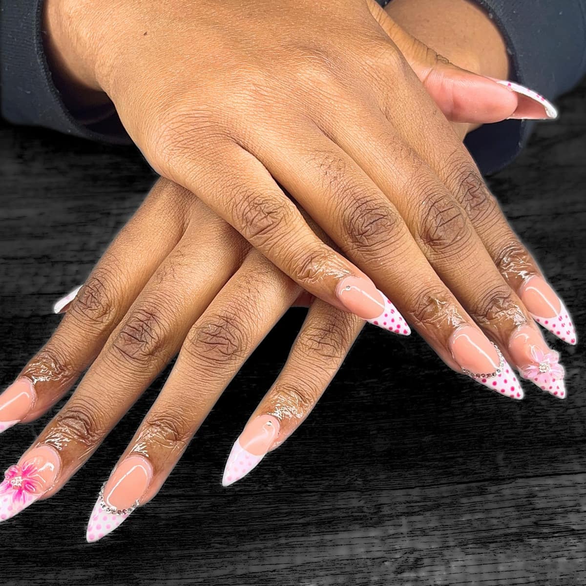 Long stiletto french in white with pink dots, a rhinestone cuff, and a sculpted pink blossom.