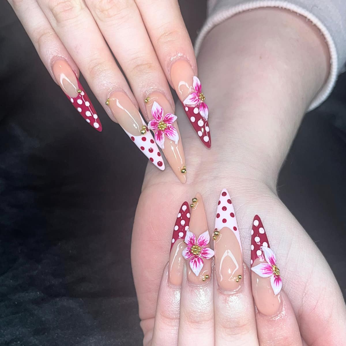 Long stiletto set with hand-painted pink lilies, red polka-dot tips, and gold bead accents.
