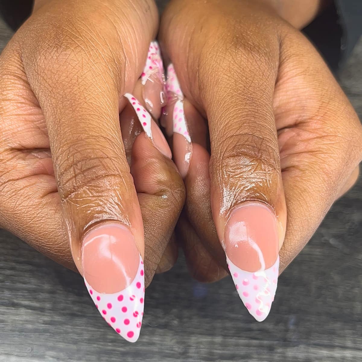 Pointed french tips in white scattered with hot pink dots, over a soft nude base.