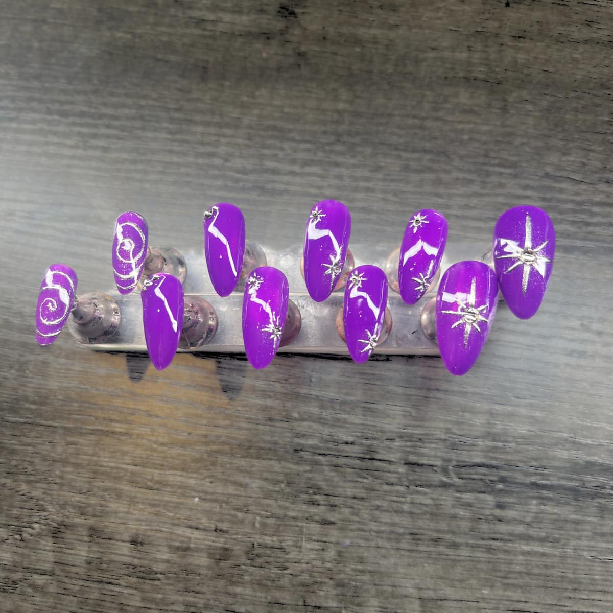 Almond press-on set in bright purple with hand-drawn silver stars and swirls.