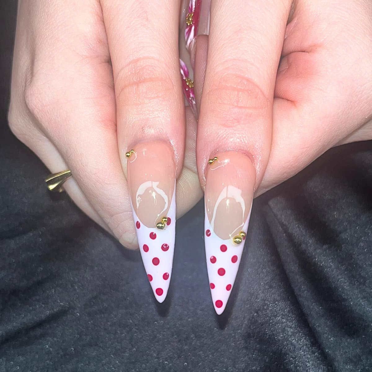 Close-up of two stiletto nails — white tips with red dots and clustered gold beads.
