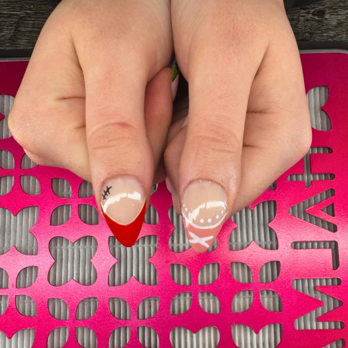 Short almond pair — one nail in red french with a fine gold line, one with a white bow and dots.